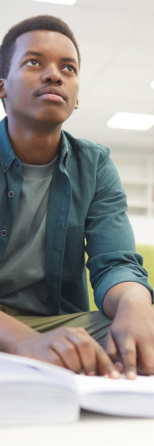 Portrait of young African-American man reading braille while studying in school library, copy space