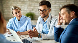 Group of healthcare workers and businessman using laptop while having a meeting in the office. Focus is on young doctor. 
